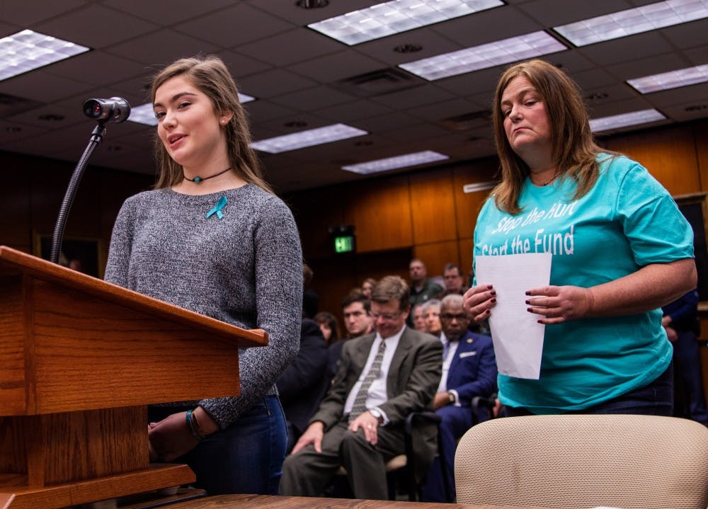 <p>Nassar survivor Emma Ann Miller speaks to the Board of Trustees during the public comment of the meeting as her mother, Leslie Miller, stands behind her Dec. 14, 2018 at the Hannah Administration Building.</p>