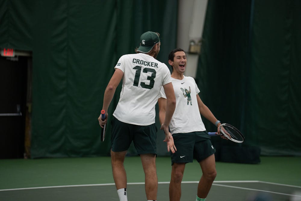 <p>Doubles partners, junior Reed Crocker and freshman Ozan Baris share a high five after scoring a point against Michigan at the MSU Tennis Center on March 30, 2023. The Spartans lost to the Wolverines 6-1.</p>