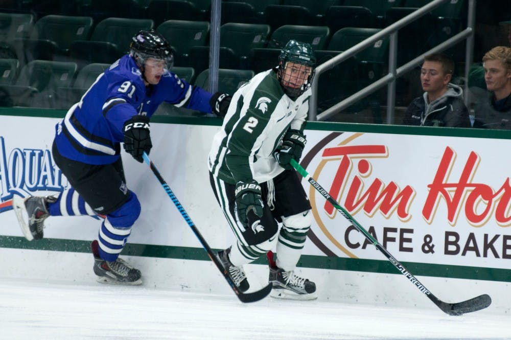 <p>Freshman defenseman Zach Osburn and Western Ontario left wing Luke Karaim chase after the puck during the exhibition hockey game against Western Ontario on Oct. 4, 2015 at Munn Ice Arena. The Spartans defeated the Mustangs, 2-1.</p>