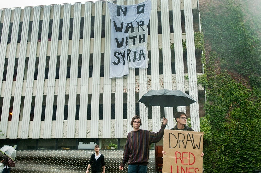 	<p>Jazz studies sophomore Duncan Tarr holds an umbrella over economics sophomore Austin Costakis during a protest demonstration against the possible war in Syria, Sept. 9, 2013, in front of the parking structure, behind Bessey Hall. The students stood in the rain to protest with a bullhorn and cardboard signs due to the impending vote by congress. Danyelle Morrow/The State News</p>