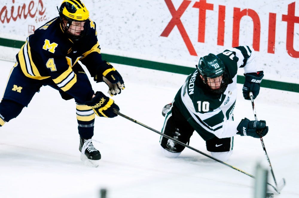 Freshman right winger Tanner Sorenson protects the puck from U of M defenseman Kevin Clare after falling to his knees Friday night at Munn Ice Arena. The spartans went on to win against the wolverines 3-2 coming back from an early lead by Michigan. Aaron Snyder/The State News.  