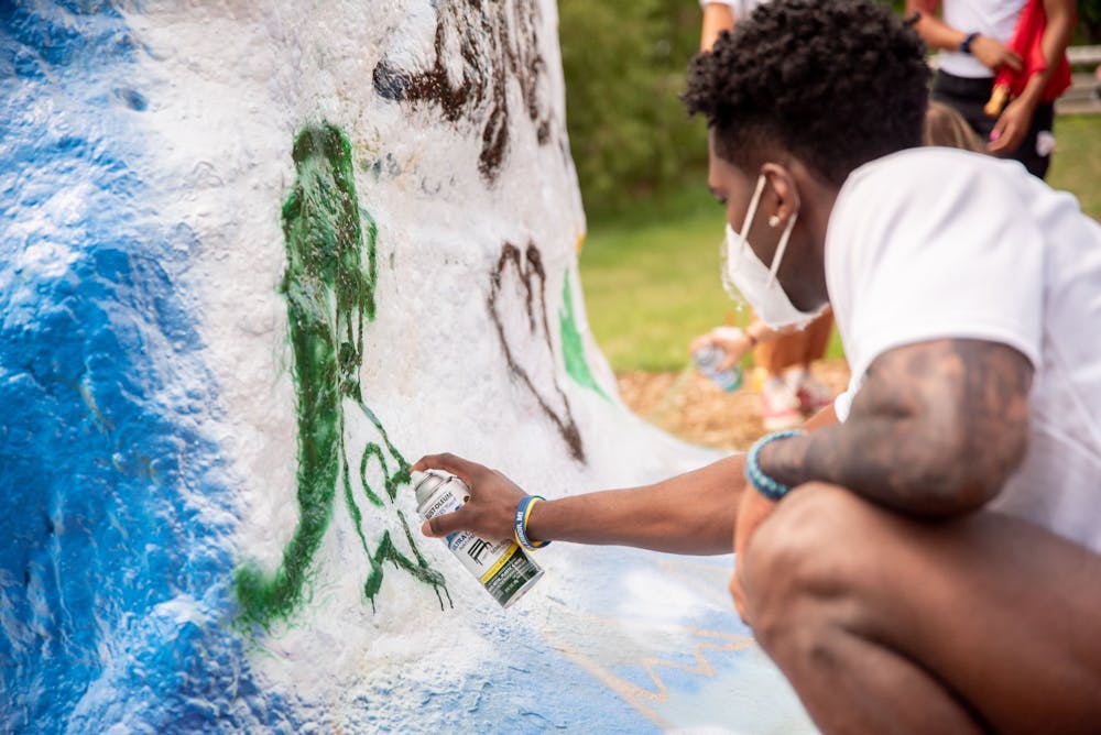 Xzavier Odom spray paints a Spartan logo onto the Rock on Farm Lane at the memorial for long jumper Tony Martin July 20, 2020. Martin died in a shooting in his hometown of Saginaw the morning of July 19. Martin held the high school state record for the long jump, with a jump of 26 feet and six inches.
