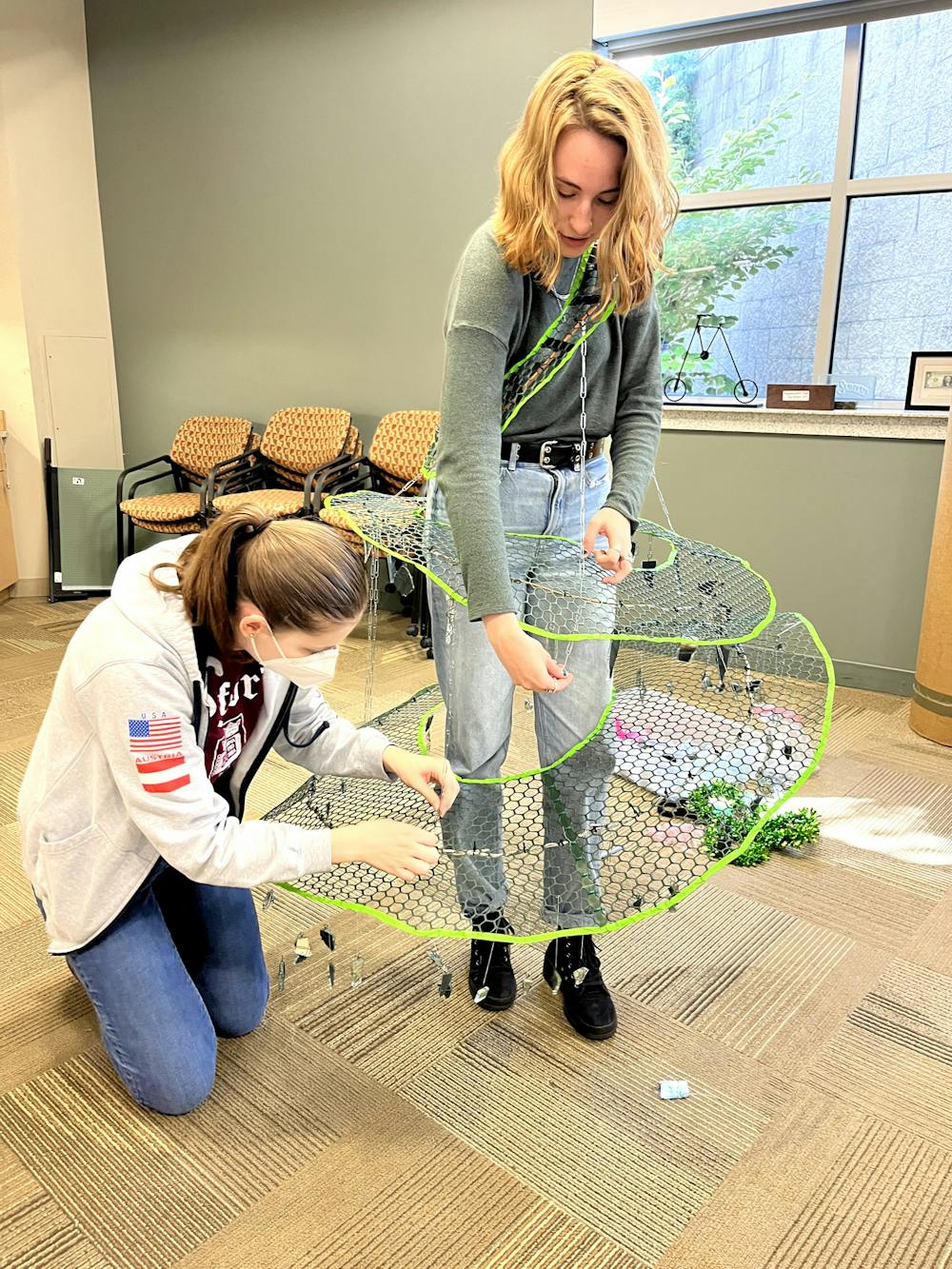 Senior arts and humanities major Alex Reeves tries on her team’s costume as teammate Carly Wholihan adjusts the paper clip fasteners. Reeves said it took a few tries to perfect the structure of the dress in order for it to stay in tact. 
