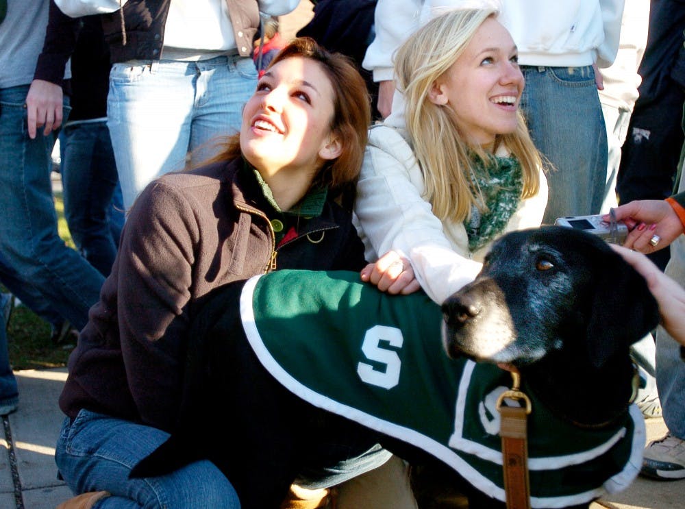 Catlin Gallagher, left, studio art sophomore, and Megan Vrobel, chemistry sophomore, on Saturday afternoon pet Zeke before the game against Penn State. Before the home football games, Jim and Terri Foley, Zeke?s owners, take the dog around to as many tailgates as they can. Zeke?s favorite tailgating food is chili. The black Labrador-pointer mix is an MSU celebrity, said owner Terri Foley, a Holland resident and Blue Cross Blue Shield case manager. ?As we?re walking around, people get 100-200 pictures taken with him on game days. They take pictures with their cell phones and all kinds of digital cameras.? Jeana-Dee Allen/The State News