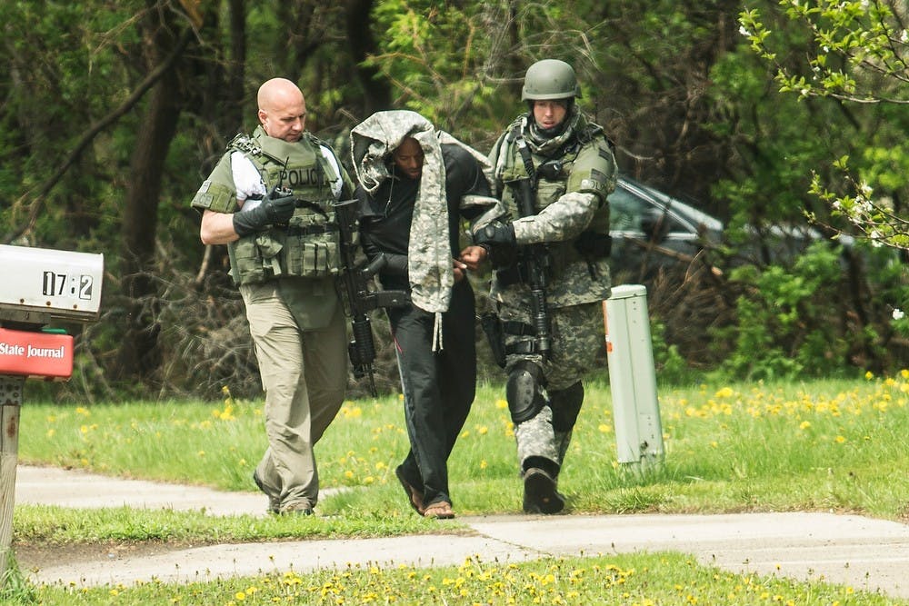 <p>Officers escort a suspect to a police vehicle May 12, 2014, outside of a home in the 1800 block of Coolidge between West Saginaw street and West Lake Lansing road. The suspect was alleged to be the same involved in the Frandor Rite Aid shooting. Danyelle Morrow/The State News</p>