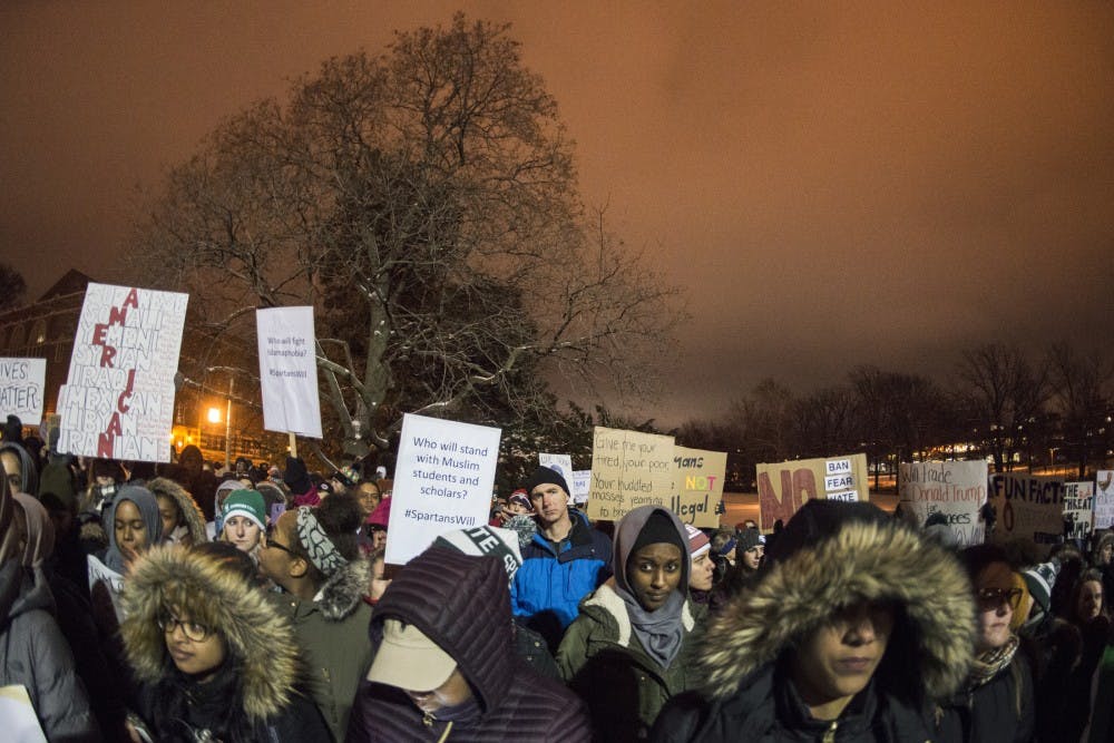 Protesters raise their posters on Jan. 31, 2017 at The Rock. The Michigan State Muslim Students' Association hosted a "No Ban, No Wall: Spartans for Sanctuary and Solidarity" as a response to President Trump's executive order on immigrants and refugees.