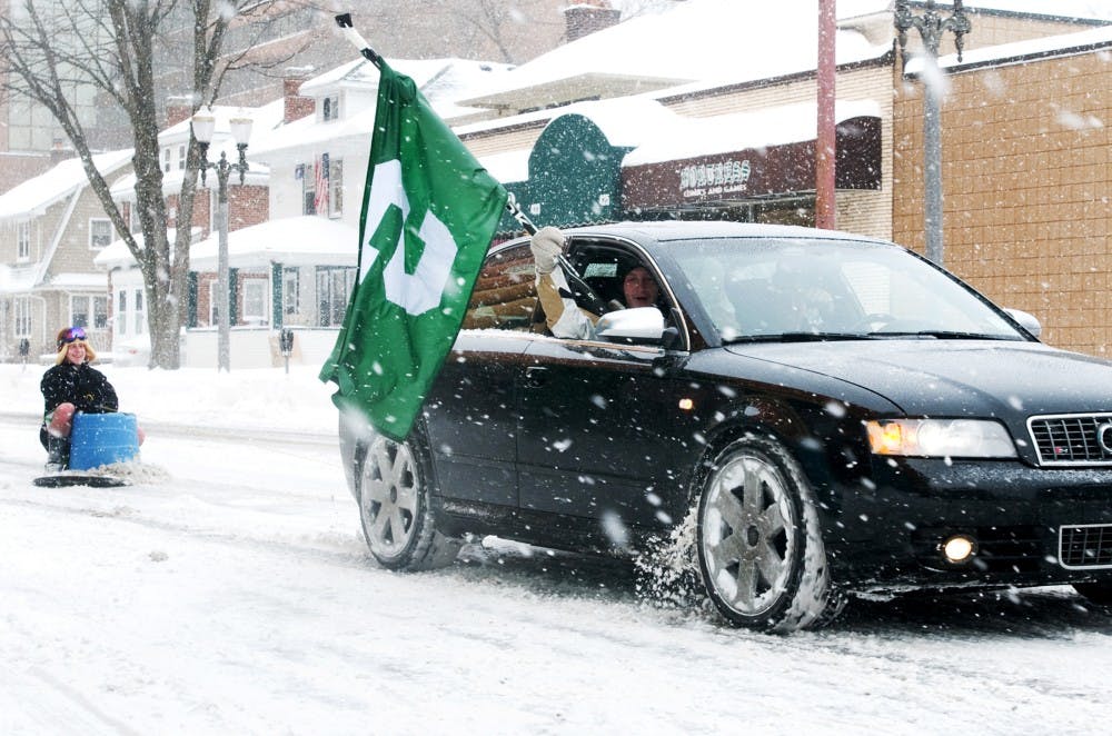 Students drive down Albert Ave. waving a Michigan State flag and pulling their friend on a sled celebrating the snow day on Wednesday morning. Classes were canceled on Wednesday for the first time since 1994 because of a winter storm. Lauren Wood/The State News