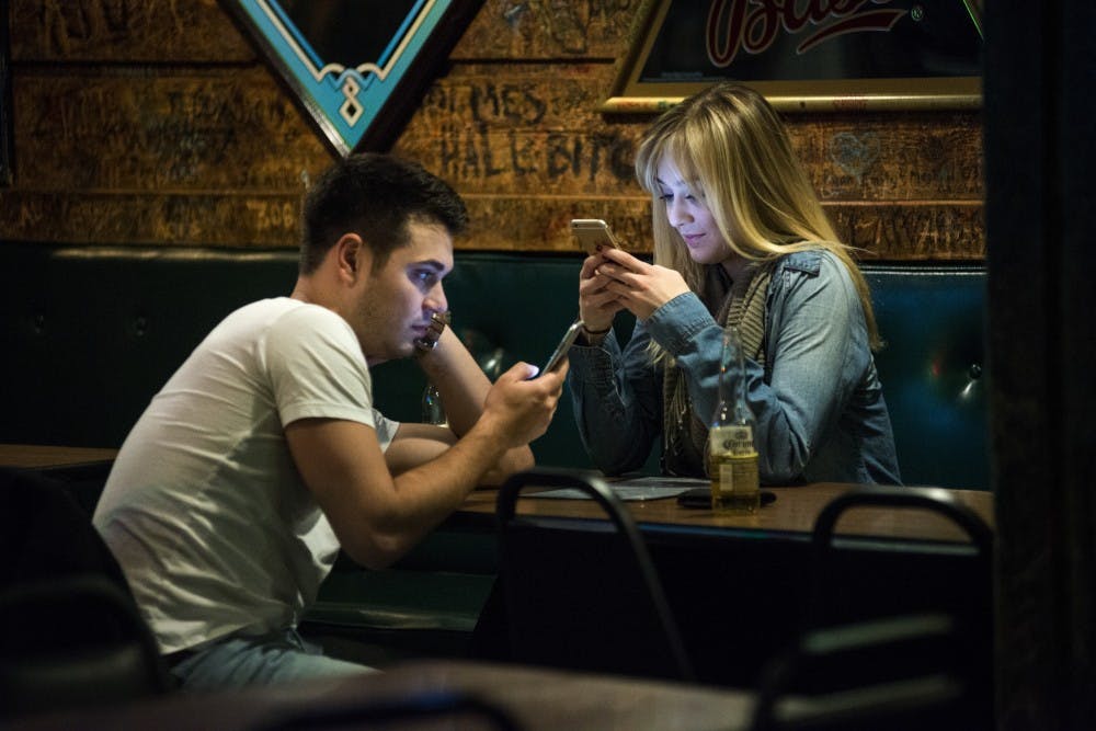 East Lansing resident Michael Cooper, left, and Macomb, Mich. resident Kayla Lopinski occupy themselves with their cellphones during Portland, Mich. resident Russ Holcomb's performance on Feb. 1, 2017 at Crunchy's at 254 E. Grand River Ave. Crunchy's has various musicians play live music every Wednesday from 10 p.m. to midnight.