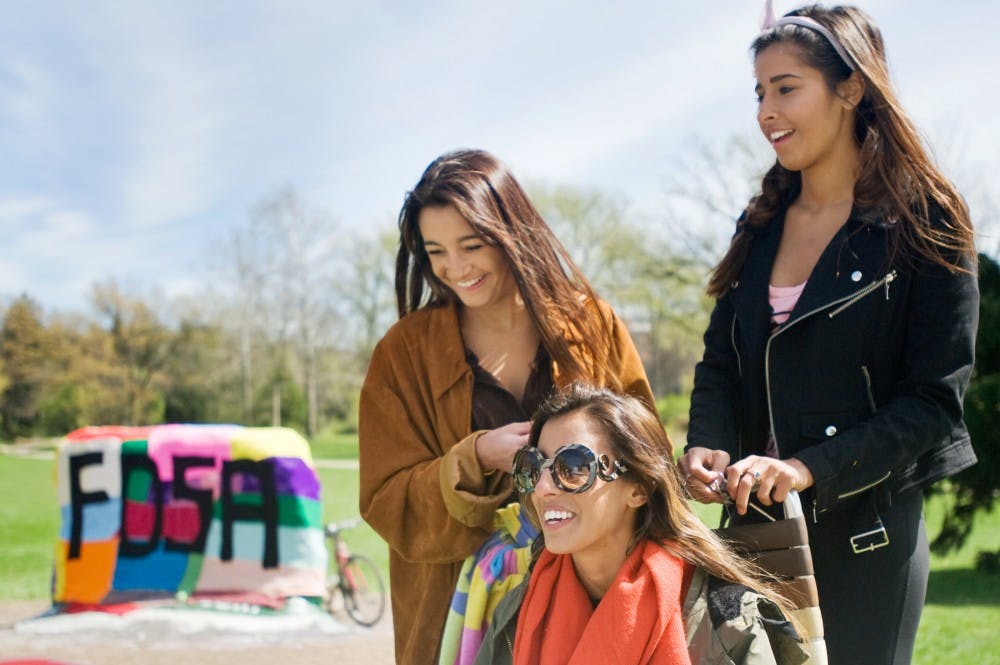 From left, Emilie Gupa, 17, stands with her sister, apparel and textile design senior Amanda McFee, and Dearborn, Mich. resident and University of Michigan-Dearborn student Aimee Gupta by the rock on Farm Lane on Wednesday afternoon, with the rock decorated with guerilla knitting. Members of Student Apparel Design Association hosted the guerilla knitting event in order to promote their club. Justin Wan/The State News