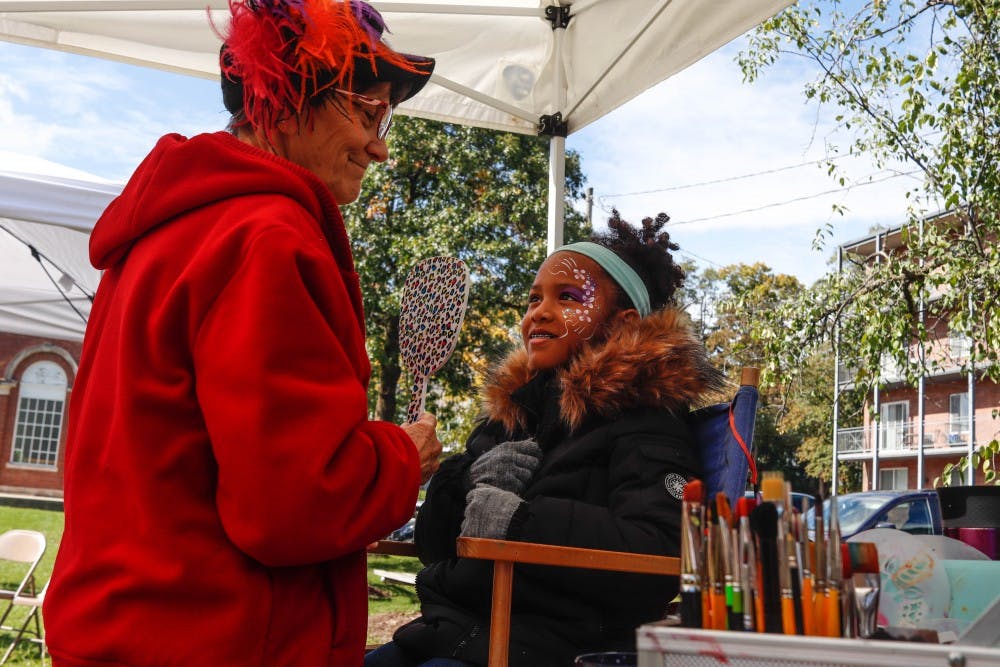 <p>Karen Miller, left, paints Madeline Huddleston’s face, right, at Autumn Fest at the East Lansing Farmer&#x27;s Market on Oct. 13, 2019.</p>