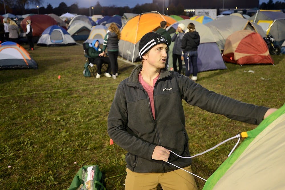 <p>Mechanical engineering junior Shannon Grace sets up his tent Oct. 17, 2014, during the Izzone Campout at Munn Field. Hundreds of students battled the cold and rain to sleep outdoors overnight in hopes of getting lower bowl seating. Julia Nagy/The State News</p>
