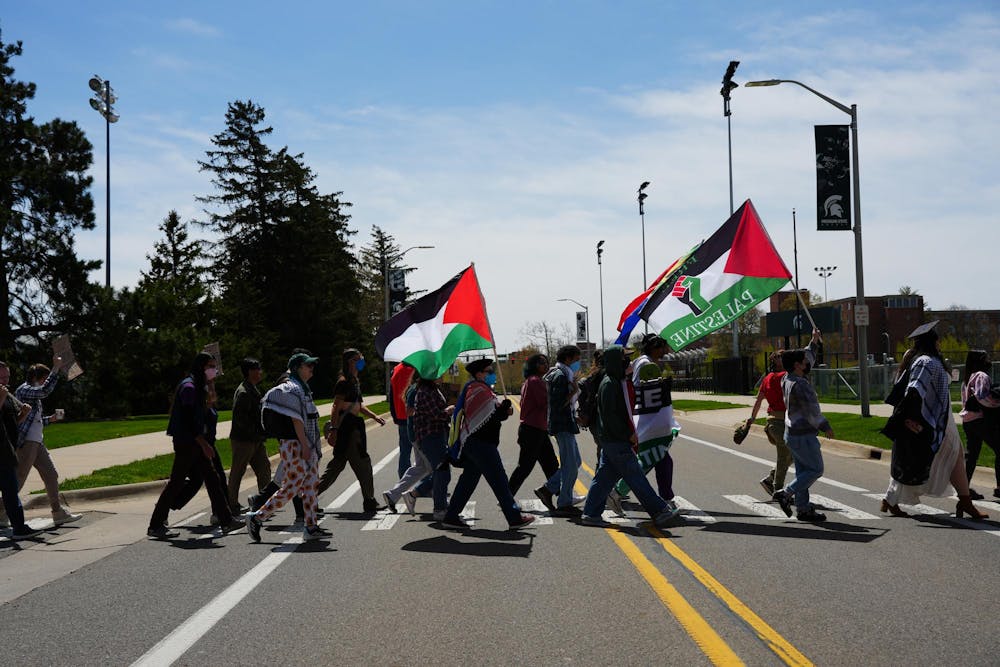 Protestors cross Chestnut Road on MSU campus as they march toward the Breslin Center on April 26, 2024. They waved Palestinian flags and chanted as they walked. 