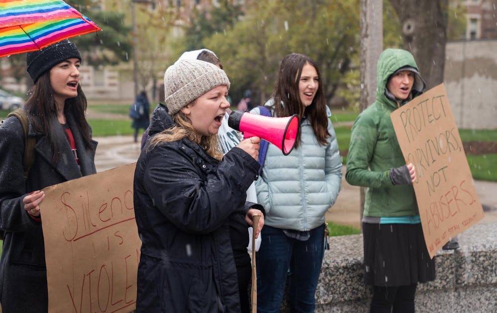 Communication senior Charlotte Plotzke speaks into a megaphone on a snowy morning in front of the Hannah Administrative Building on Tuesday, April 25, 2023. Students gathered to protest the Board of Trustee’s refusal to release documents about the university’s response to Larry Nassar’s sexual abuse cases.