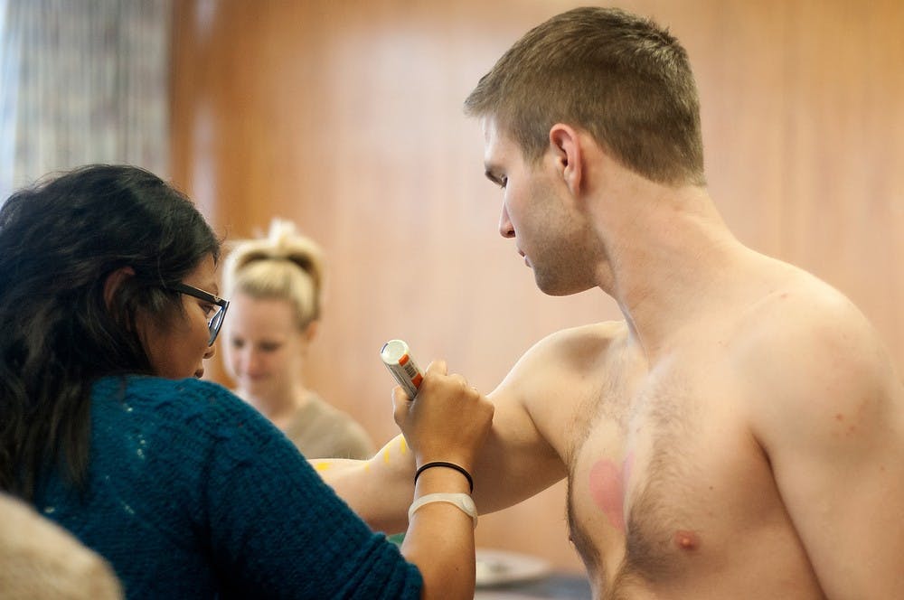 <p>Human biology junior Apa Flores draws body art on supply chain management junior Blair Pitcairn before the Stride for Pride run on March 25, 2014 at Shaw Hall. This was Pitcairn's third year doing Stride for Pride. Betsy Agosta/The State News</p>