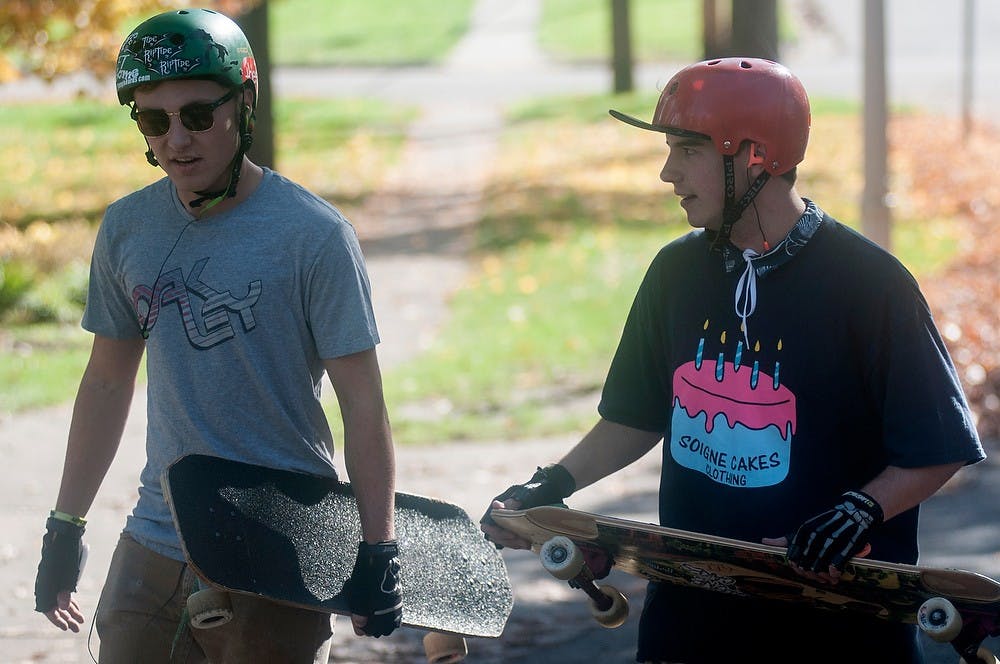 <p>Mechanical engineering freshman Evan Finses, left, and computer science freshman Turner Anderson carry their longboards up the road Oct. 23, 2014, on Center Street by Michigan Avenue. Both Finses and Anderson longboard on this street almost everyday during the week. Raymond Williams/The State News</p>