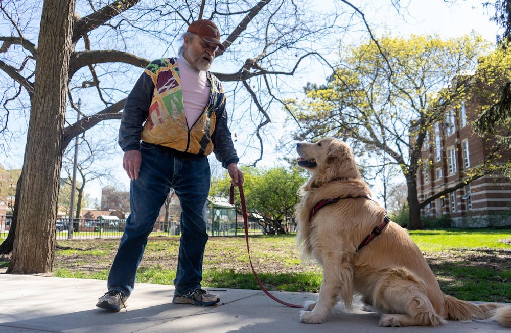 Mike Harju and his dog Raymond stand along Grand River Avenue on April 22, 2024. 