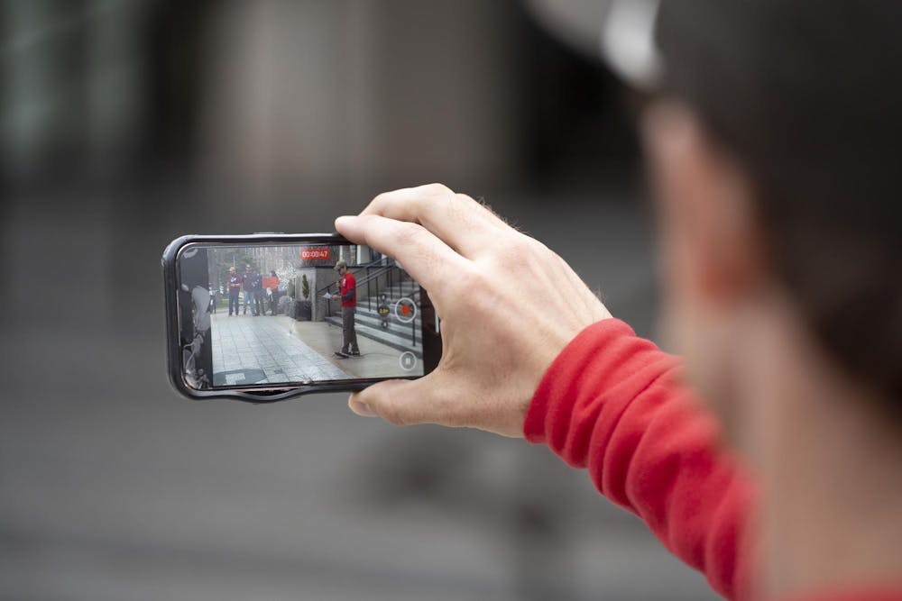 A participant films a speaker on their phone during the Stand Up for Higher Education Rally outside the Hannah Administration Building on April 17, 2025.
