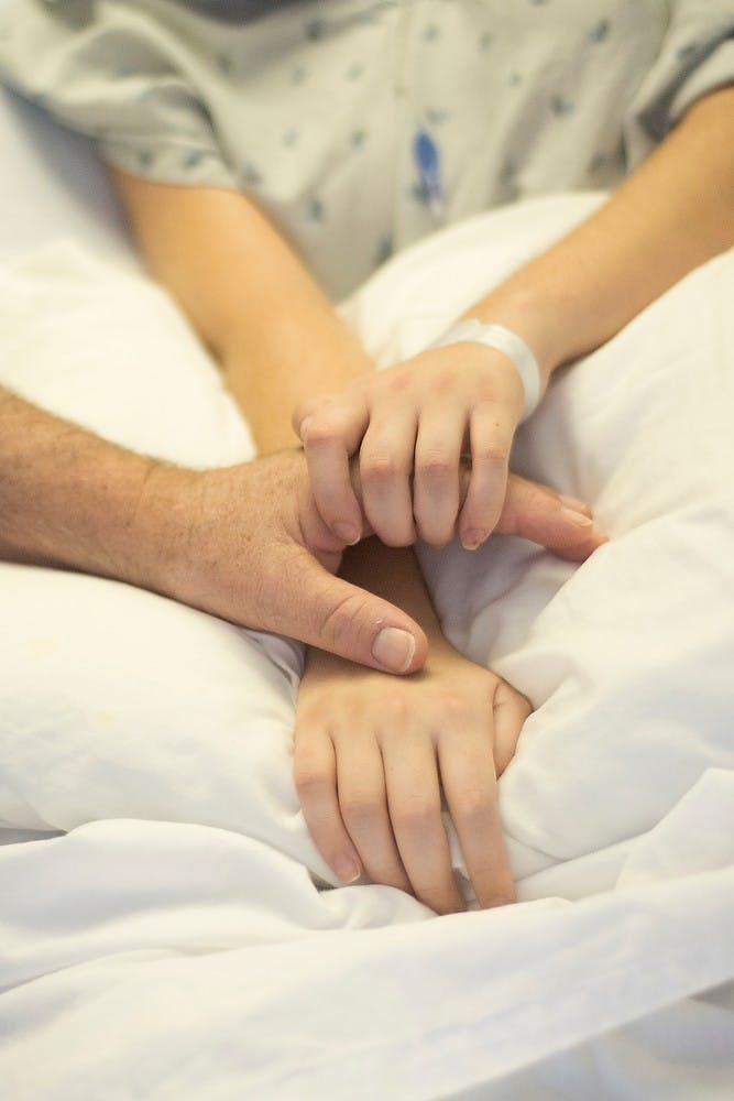 <p>Dale Blakeslee holds onto his daughter's hands, MSU graduate Stacy Blakeslee, on March 14, 2014, at Spectrum Rehab and Nursing Center, 4118 Kalamazoo Ave., in Grand Rapids. Dale tries to come up on weekends to visit his daughter. During his visit, Stacy wouldn't let go of his hand. Julia Nagy/The State News</p>