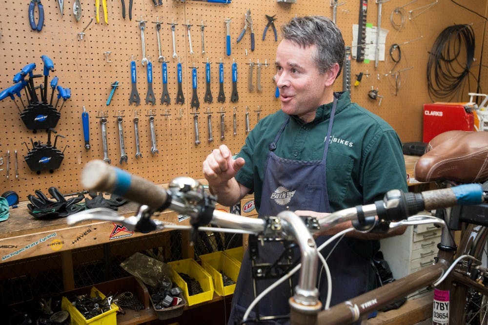 Williamston Mich., resident and MSU faculty member Layne Cameron speaks to a student on Dec. 9, 2015 in the basement of Demonstration Hall. The MSU volunteer bike shop is open to all students and faculty who present an MSU ID. 