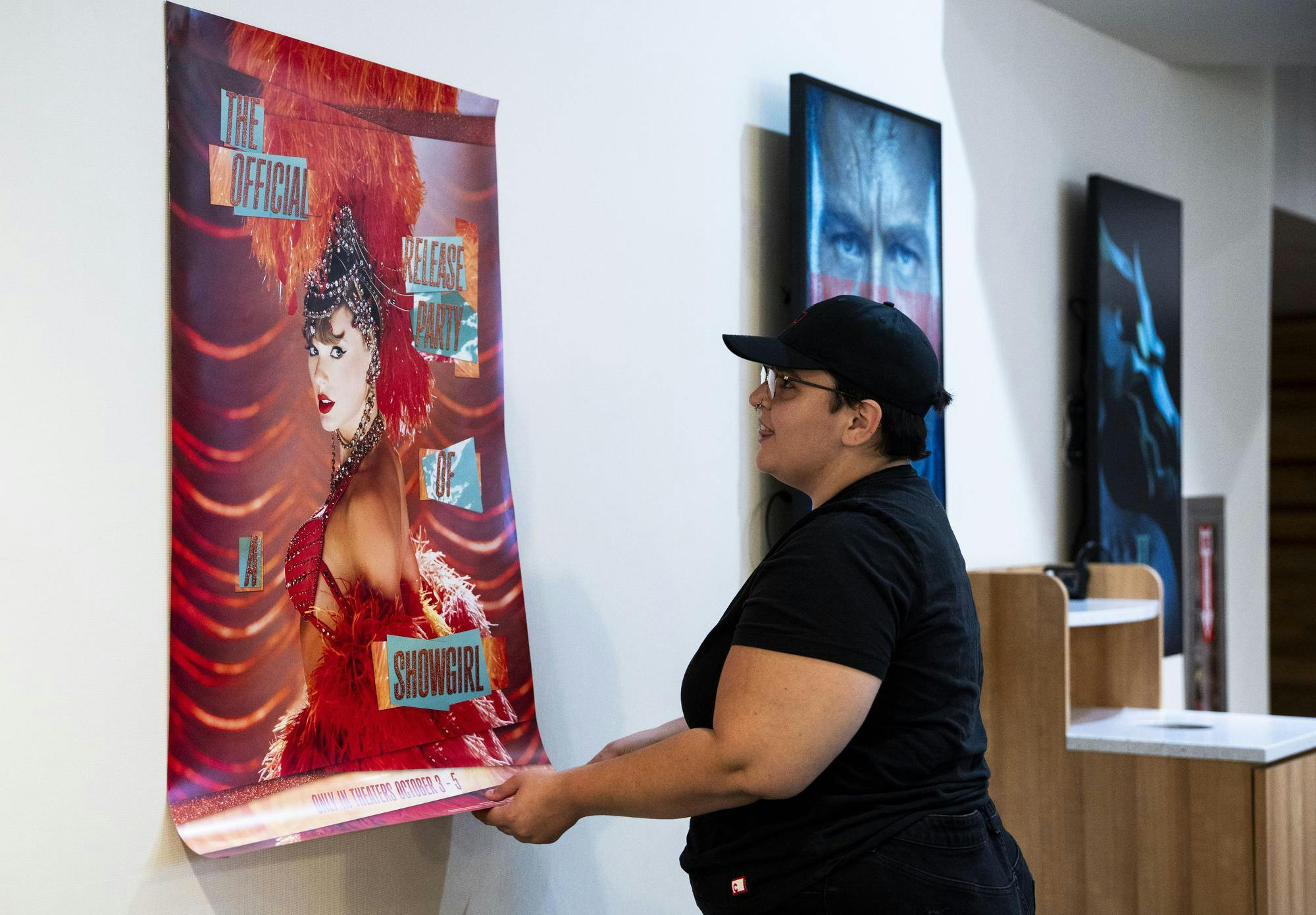 The manager at Studio C! Theater in the Meridian Mall, Lauren Chavez, hangs up a poster for Taylor Swift' s new movie The Life of a Show Girl on Oct. 1, 2025. 