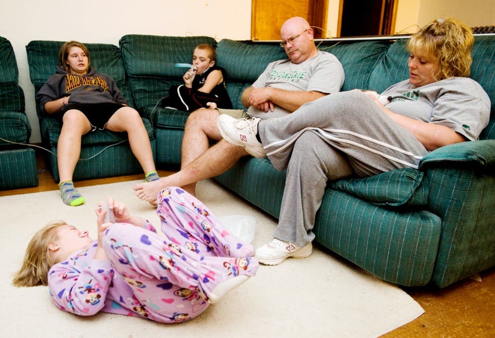 Misty Holley, far right, of Fowlerville sits with her husband Larry, son Kristopher Brookens-Hillebrand, 14, and step-daughter Gabbie Holley, 13, as her daughter Dakota Brookens-Hillebrand, 12, laughs on the ground in their home Sunday night. Kristopher was using his nebulizer to help with his asthma. Lauren Wood/The State News