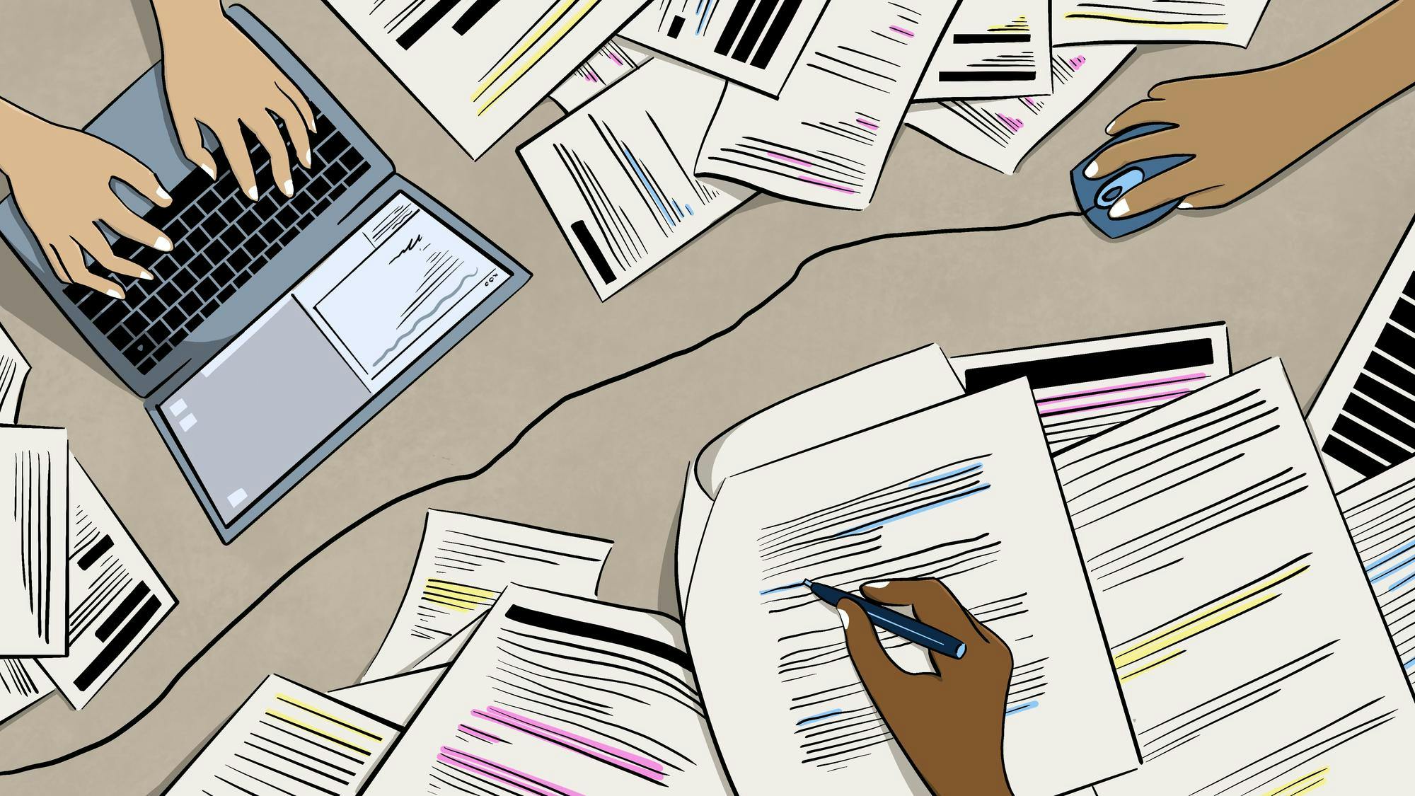 Hands are working on a laptop while surrounded by numerous papers with various colored markings.