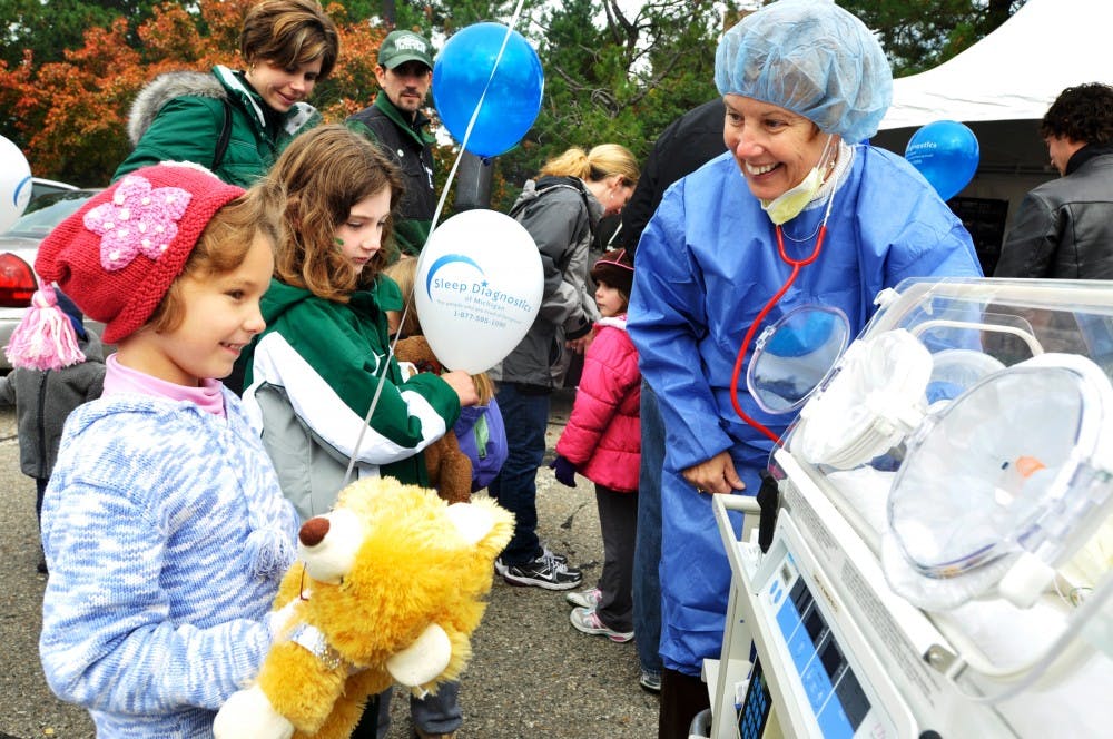 From left, Kayla Michael, 6, of Lansing, and Leisya Newell, 6, of Williamston, Mich., gaze at a new born baby cart as Sparrow Hospital nurse Suzegge Wasielewski invites the children to touch the teddy bear inside the cart. The College of Human Medicine hosted the Teddy Bear Hospital and Picnic 4H Children?s Garden Saturday noon time.  Justin Wan/The State News
