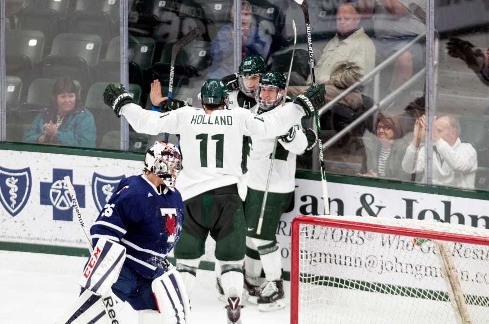 Redshirt-senior defenseman Rhett Holland (11) joins teammates to celebrate after the the Spartans opened the scoring during an exhibition game against the University of Toronto on Oct. 2, 2016 at Munn Ice Arena. The Spartans defeated the Blues 2-1 in an overtime shootout after ending regulation in a 2-2 tie. 