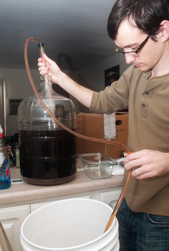 Microbiology senior Patrick Ropp transfers his homemade beer from the fermenting container to a bucket in order to bottle the beer on Saturday, Feb. 23, 2013, at his apartment in East Lansing. Ropp named the hibiscus-flavored brew "Prix de Fleur," a pun on a fencing term. Danyelle Morrow/The State News