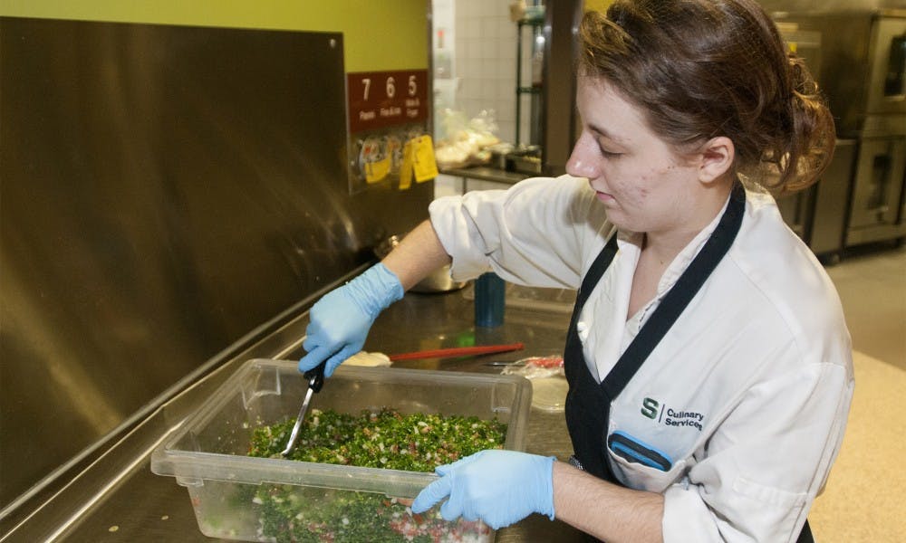 <p>MSU alumna Samantha Van Atta prepares tabouli on Sept. 2, 2015, at the Veg Out station inside Brody Cafe. Atta sympathizes with the students who live on campus and have restricted diets. "I think it's nice that we have a vegetarian option," Atta said.</p>