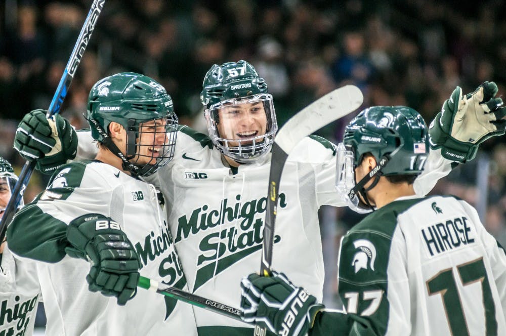 Redshirt sophomore defenseman Jerad Rosburg (57) celebrates a goal with sophomore forward Patrick Khodorenko (55) and sophomore forward Taro Hirose (17) during the game against Michigan on Dec. 6, 2017, at Munn Ice Arena. The Spartans defeated the Wolverines, 5-0.