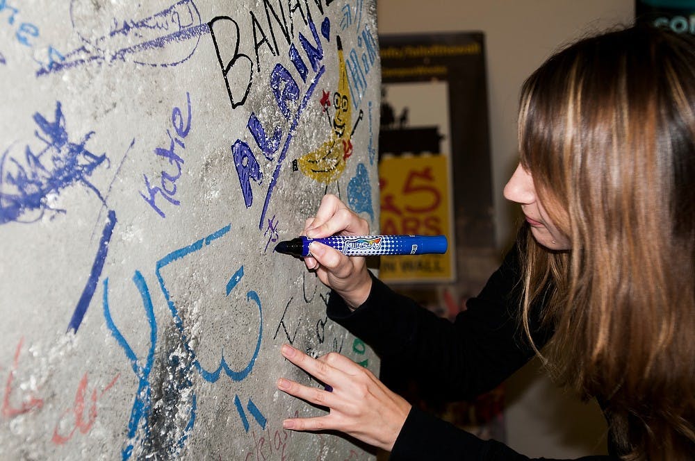 <p>Marketing and Japanese senior Kristen Lotrey writes a message in Japanese on the replica Berlin Wall on Oct. 27, 2014, at Wells Hall for the 25th anniversary of its destruction. The installment features two interactive kiosks with information regarding the wall's history. Dylan Vowell/The State News</p>