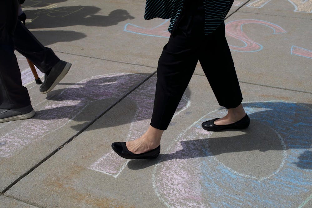 A woman walks across the words "denounce" and "divest" after convocation on April 26, 2024. After protestors left, the area filled with people celebrating graduation. 
