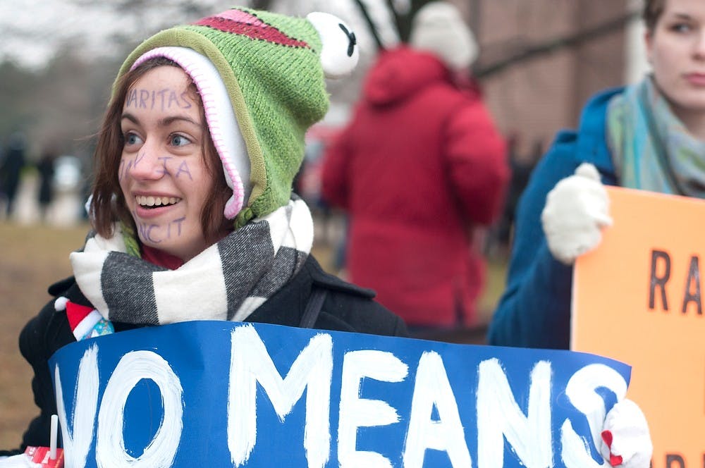 <p>Comparative culture and politics sophomore Alexa Kirsch joins her fellow protesters Dec. 13, 2014 during a protest against commencement speaker, George Will outside of Breslin Center. On her face she wrote "veritas omnia vincit" which means truth conquers all in latin. Jessalyn Tamez/The State News </p>