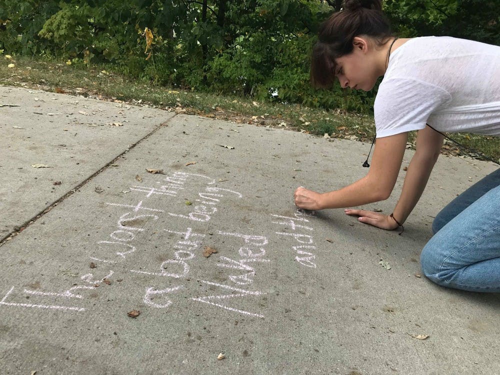 <p>A student writes a poem in chalk on the sidewalk of the trail behind Shaw Hall on Sept. 19.&nbsp;</p>