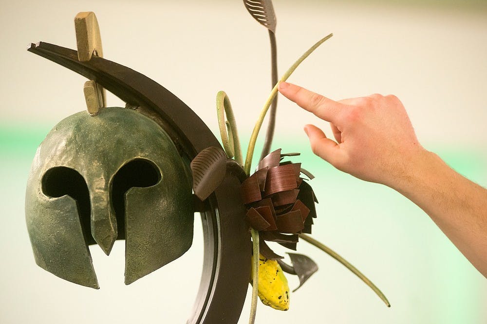 	<p>Justin Raha, a baking and pastry arts instructor at the Culinary Institute of Michigan, points to and explains his winning piece at the 25th Annual Chocolate Party Benefit on Feb. 23, 2014, at the Kellogg Center. The benefit fundraises money for the <span class="caps">MSU</span> Museum. </p>