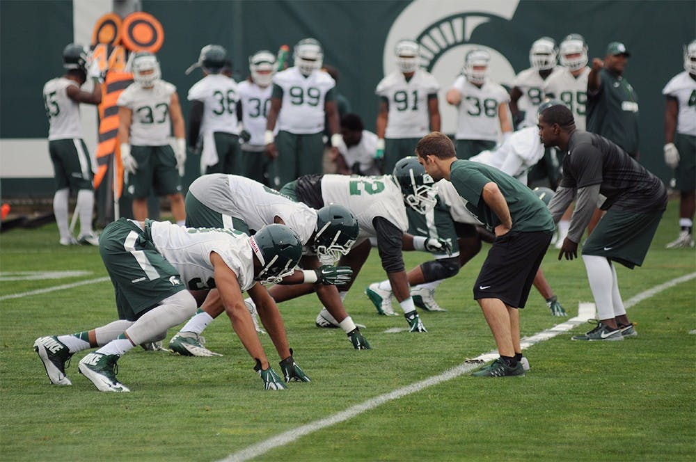 <p>Defensive line players line up to take a snap next to the Duffy Daugherty Football Building on August 8, 2015 during the first practice of fall. Joshua Abraham/The State News</p>