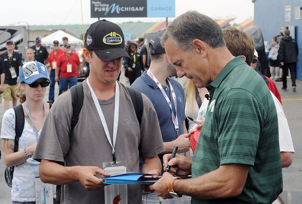 <p>Head football coach Mark Dantonio signs an autograph for a fan at the NASCAR Sprint Cup Series Quicken Loans 400 on June 14, 2015, at Michigan International Speedway in Brooklyn, Mich. Dantonio served as the grand marshal for the race. Joshua Abraham/The State News</p>
