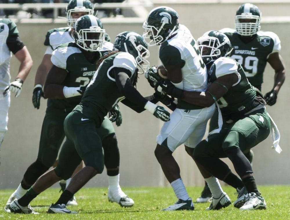 <p>Then-junior cornerback Trae Waynes, left, and then-redshirt freshman linebacker Shane Jones tackle then-junior wide receiver DeAnthony Arnett during the Spring Green and White game on April 26, 2014, at Spartan Stadium. The White team, coached by defensive line coach Ron Burton, defeated the Green team, 20-13. Danyelle Morrow/The State News</p>