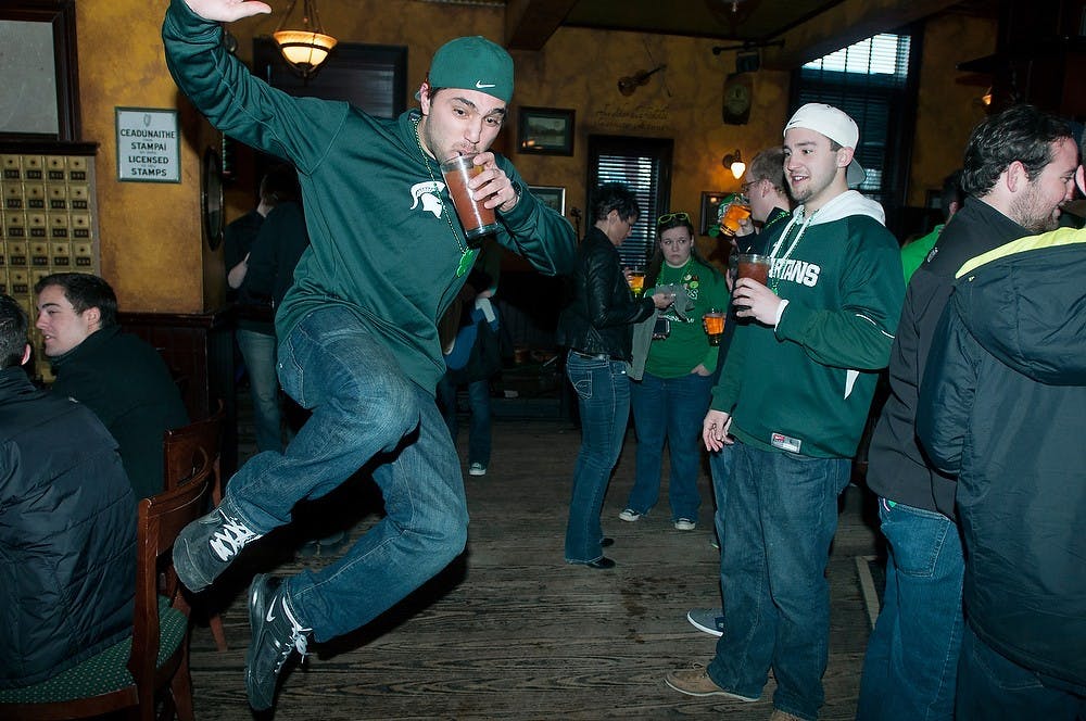 <p>Human resources senior Jimmy Martinez jumps on March 17, 2014, around 7 a.m. in Dublin Square Bar. Martinez said he was happy to spend the morning of St. Patrick&#8217;s Day drinking with friends. Allison Brooks/The State News</p>