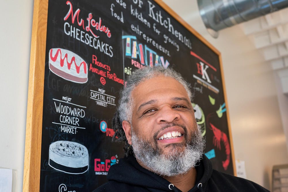 <p>Marcus Leslie Sr., owner of Mr. Leslie’s Cheesecakes, standing in front of a board promoting his business in Lansing on Feb. 23, 2024.</p>