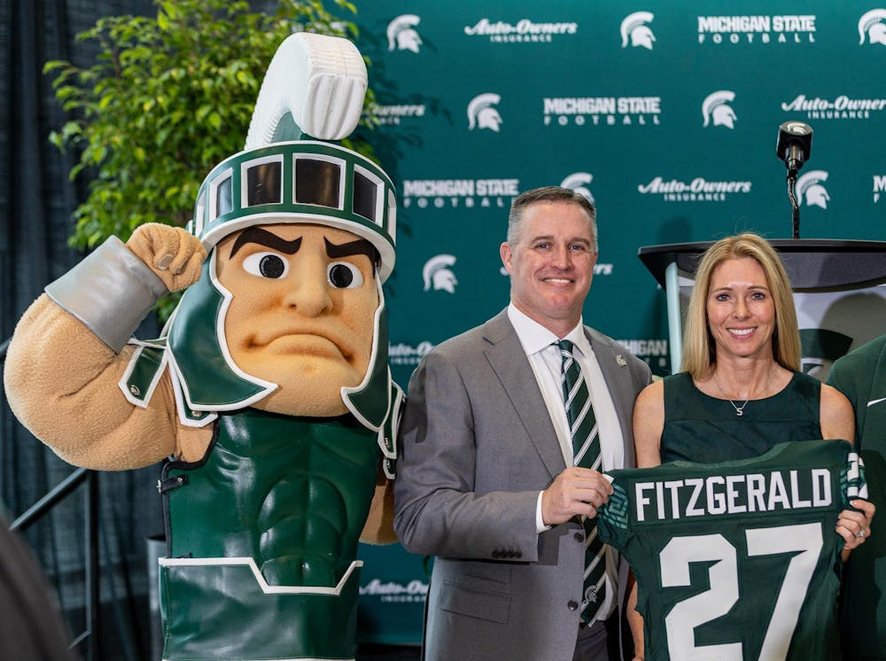 Michigan State University's new football HC Pat Fitzgerald  poses with his wife, Stacy Fitzgerald and Sparty while holding his new spartan jersey in the Tom Izzo football building in East Lansing, MI on Dec. 2, 2025.