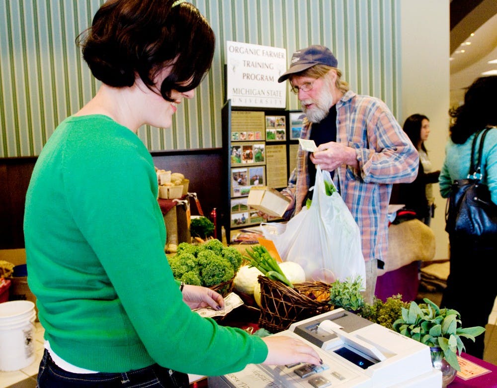 Katherine Moore, farm stand manager and an assistant instructor with Student Organic Farms, sells produce to Lansing resident John Hooper, also president of Michigan Organic Food and Farm Alliance, Saturday at The Land Grant held in the previous Barnes and Noble location on Grand River Ave. Local farmers were able to sell produce to the public at various booths set up in the building. Jaclyn McNeal/The State News
