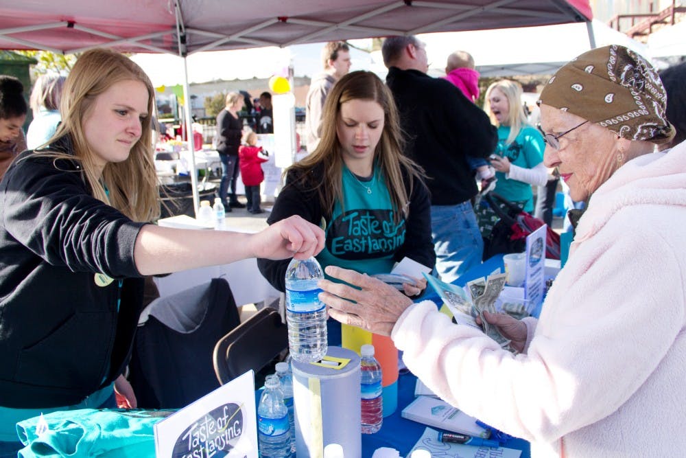 Communications senior Catie Musatics hands a water to East lansing resident, Carilyn Padgitt during the first-ever Taste of East Lansing event hosted by the city of East Lansing's Community Relations Coalition Saturday evening at Ann Street Plaza The event featured local food vendors, games, arts & crafts. Aaron Snyder/The State News 