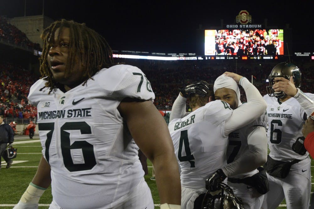 <p>Senior offensive lineman Donavon Clark, 76, walks off the field as junior kicker Michael Geiger, 4, hugs freshman safety Khari Willis after the game against Ohio State on Nov. 21, 2015 at Ohio Stadium in Columbus, Ohio. The Spartans defeated the Buckeyes, 17-14.</p>