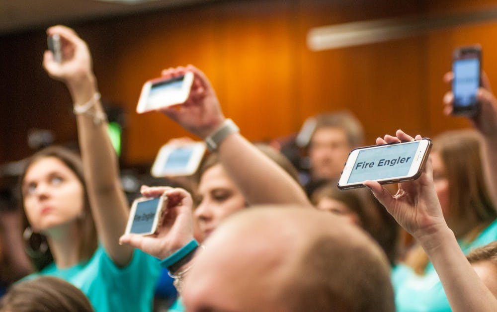 Members of the community and Reclaim MSU hold up devices reading “Fire Engler” at the Action Meeting of Board of Trustees at the Hannah Administration Building on June 22, 2018.