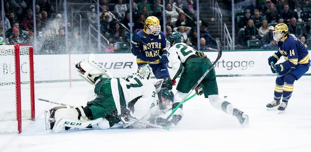 <p>Graduate student goalie Dylan St. Cyr (37) falls on fifth-year defender Cole Krygier (8) as he tries to make the save during a game against Notre Dame at Munn Ice Arena on Feb. 3, 2023. The Spartans defeated the Fighting Irish 3-0.</p>