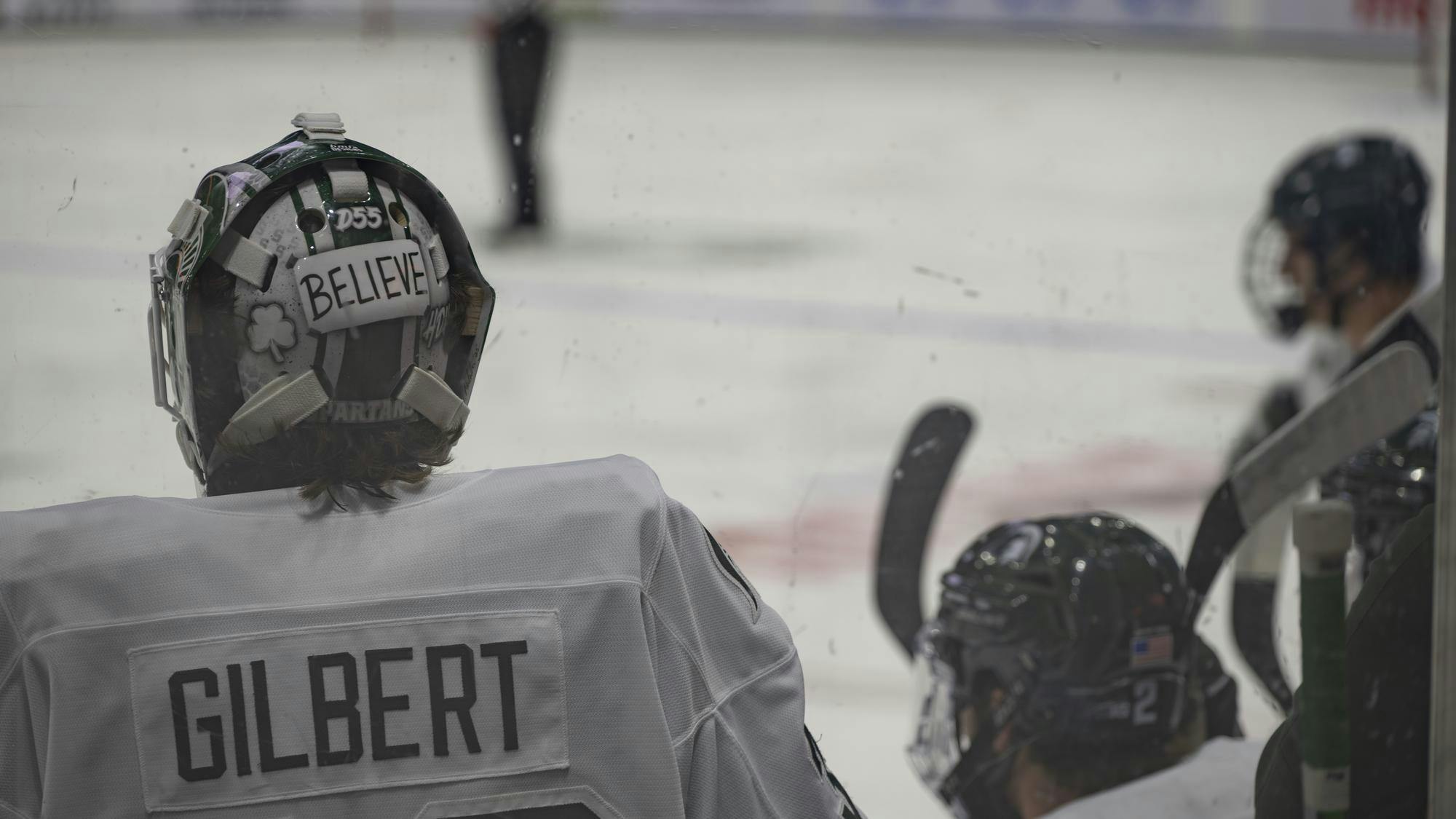 <p>Dolan Gilbert (Sr., Goalie) watches the game from the bench, his helmet emblazoned with the word “Believe,” at Munn Ice Arena on Oct. 10, 2025</p>