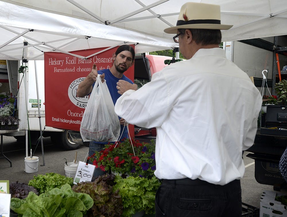 <p>Nicholas Corrion of Corrion Family Farms assists a customer making a purchase at this year's opening day of the East Lansing Farmer's Market June 6th, 2015 in Valley Court Park. Wyatt Giangrande/State News</p>