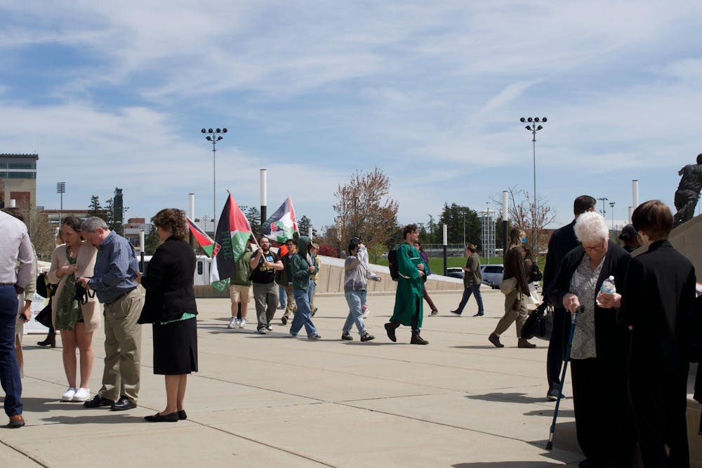 People attending spring convocation stand near student protestors outside the Breslin Center on April 26, 2024. The students picketed the event, demanding MSU divest from Israel.